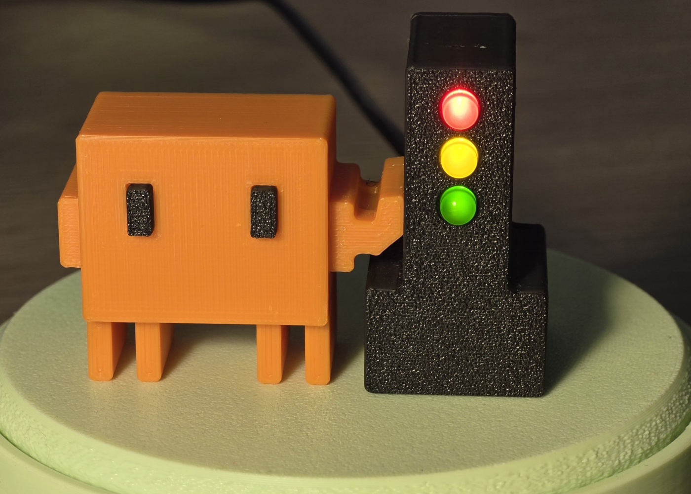 BroGlow’s orange mascot beside the black traffic light with all three LEDs glowing red, yellow and green